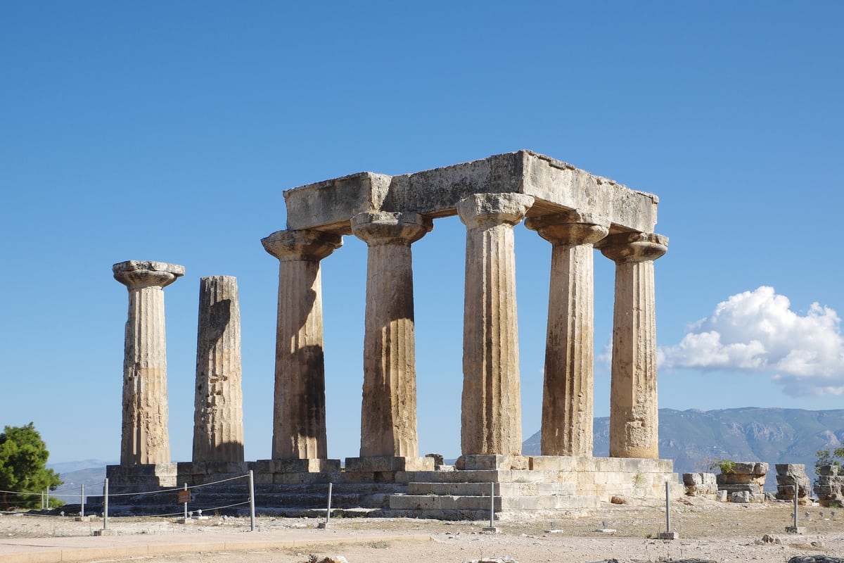 An Ancient Corinth tour stands before the seven Doric columns of the Temple of Apollo under a clear sky