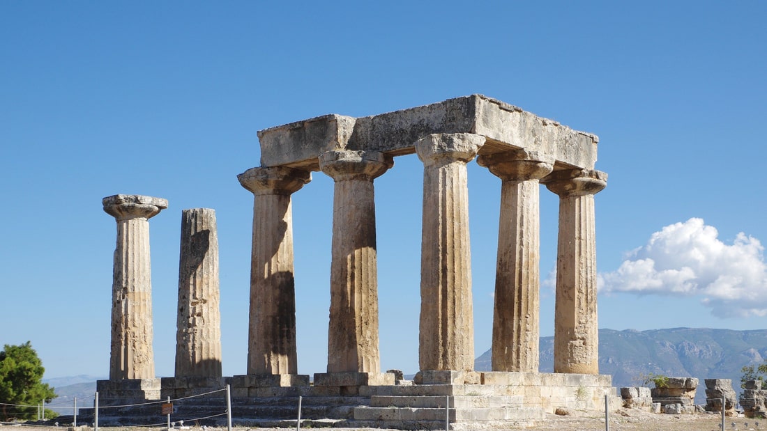 An Ancient Corinth tour stands before the seven Doric columns of the Temple of Apollo under a clear sky