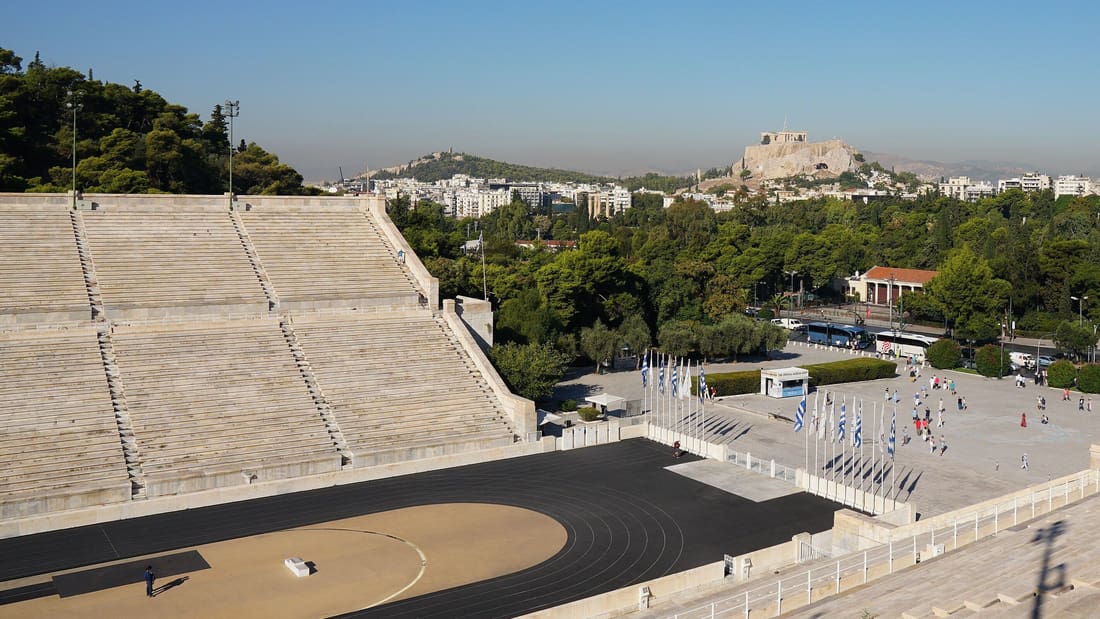 An Athens bike tour stops at the marble Panathenaic Stadium, with the Acropolis rising beyond the trees