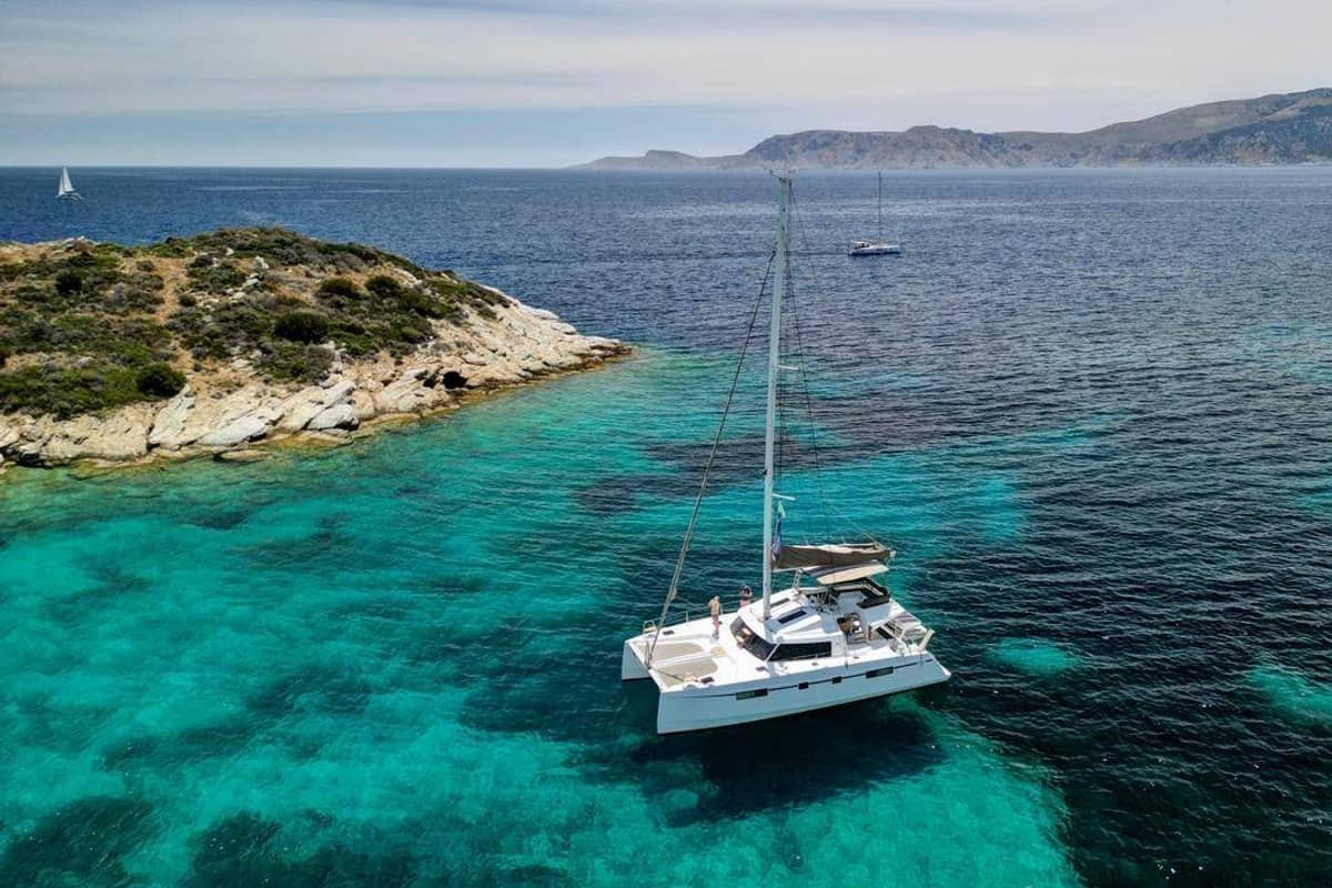 A sailing catamaran anchored in turquoise water off a small islet of the Athens Riviera on an Athens catamaran cruise