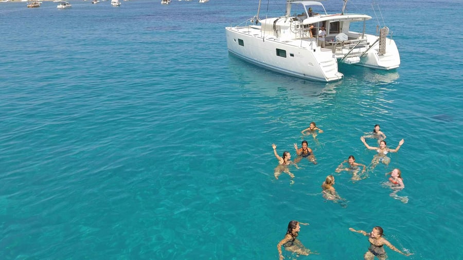 An Athens Riviera cruise swim stop, with guests swimming in clear turquoise water beside a white catamaran