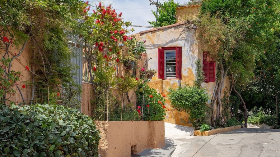 An Athens walking tour climbs through Anafiotika, past old houses with red shutters and flowering gardens