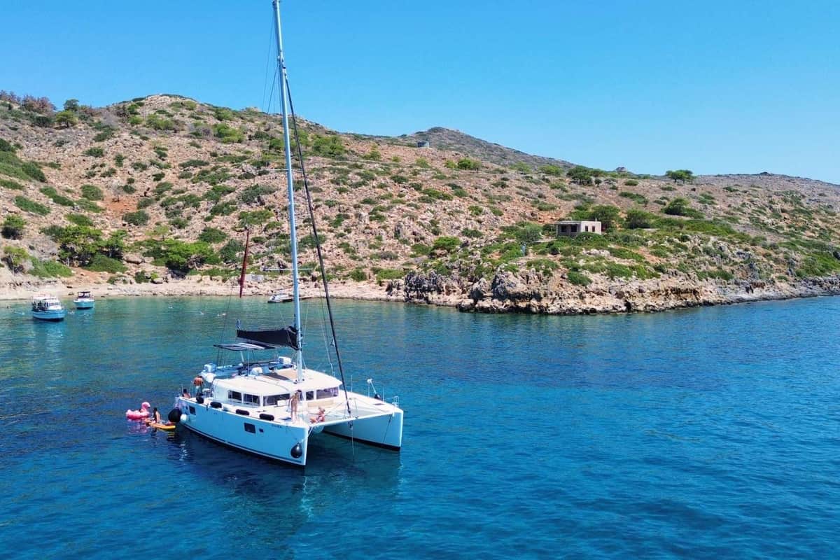 Chania catamaran cruise boat anchored in clear blue water off the rocky shore of an islet
