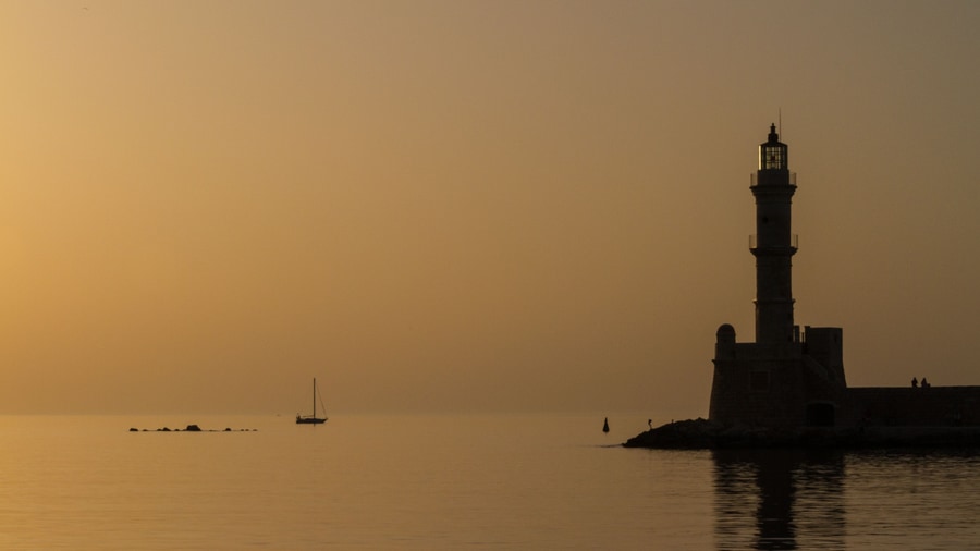 A sailing boat off the Venetian lighthouse of Chania at sunset, the light a Chania sunset cruise sails into