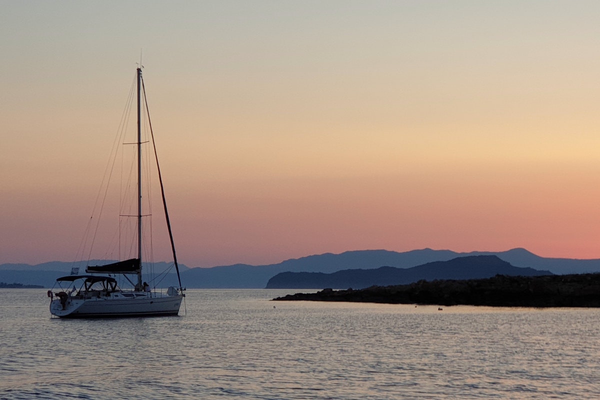 A Chania sunset cruise yacht at anchor on a calm sea off Chania as the sky turns pink behind the mountains of western Crete