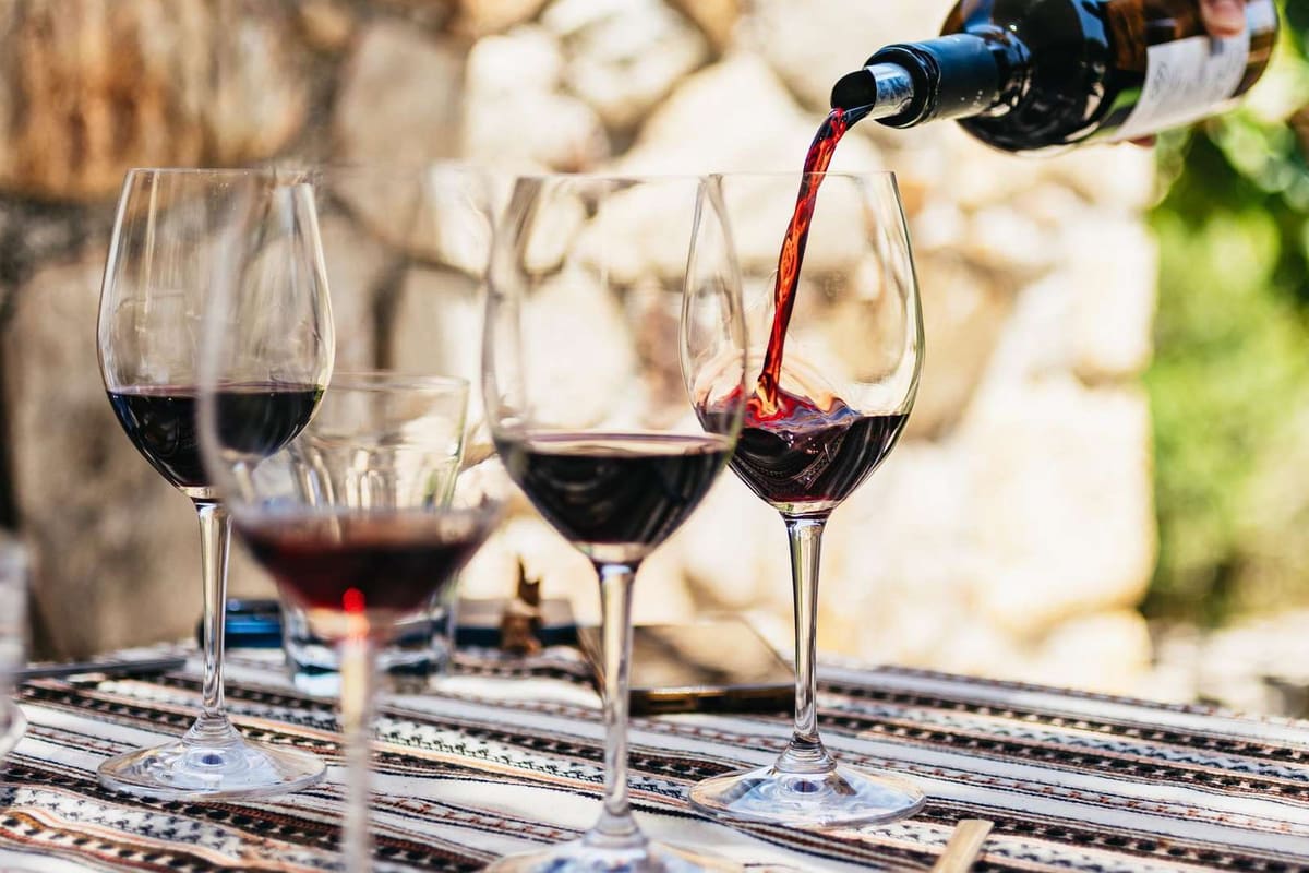 Chania wine tour tasting, red wine poured into glasses on a woven tablecloth beside a stone wall