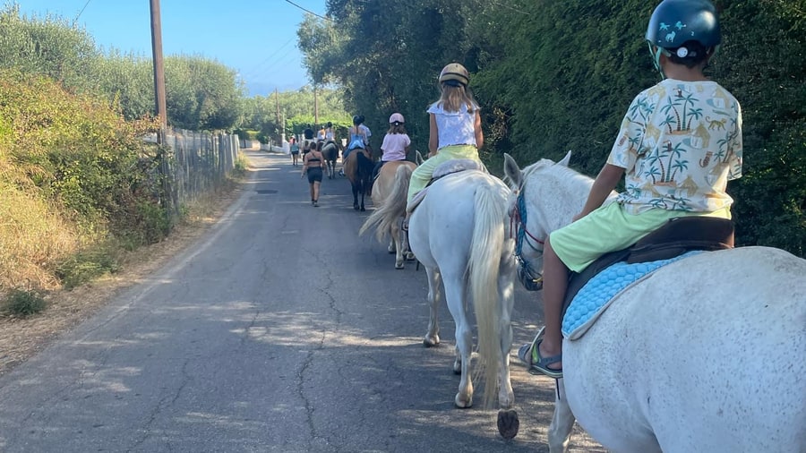 Young riders in helmets on white horses on a Corfu horse riding tour along a green country lane