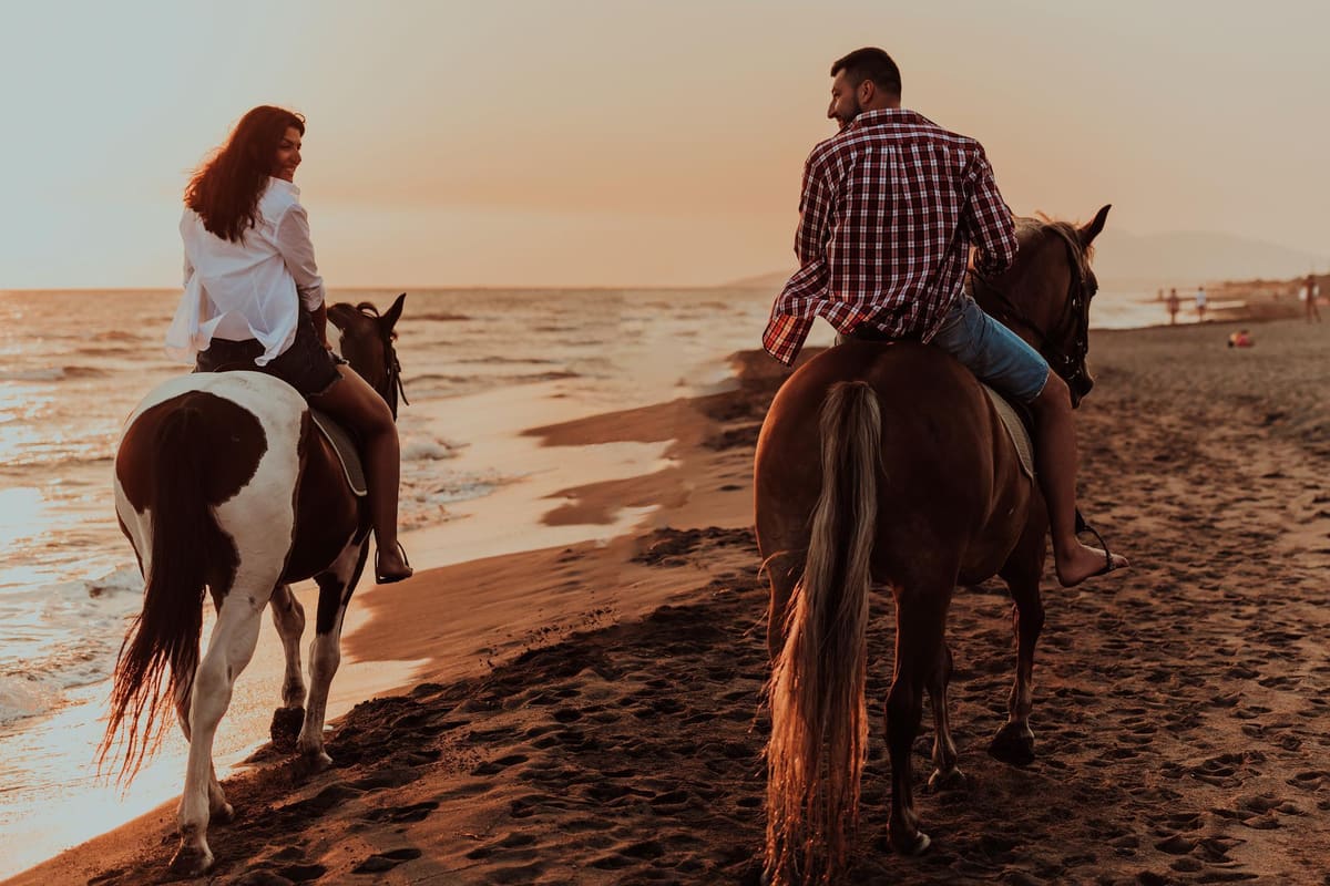 Corfu horse riding at golden hour, with two riders on a brown horse and a paint horse walking along a sandy beach