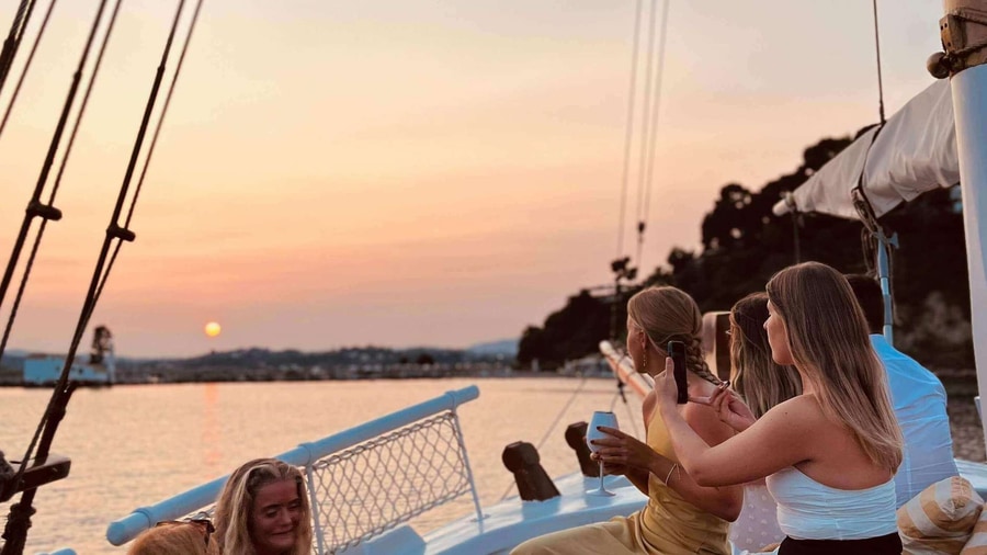 Guests on the deck of a classic sailing boat watch the sun set over the sea on a Corfu sailing tour