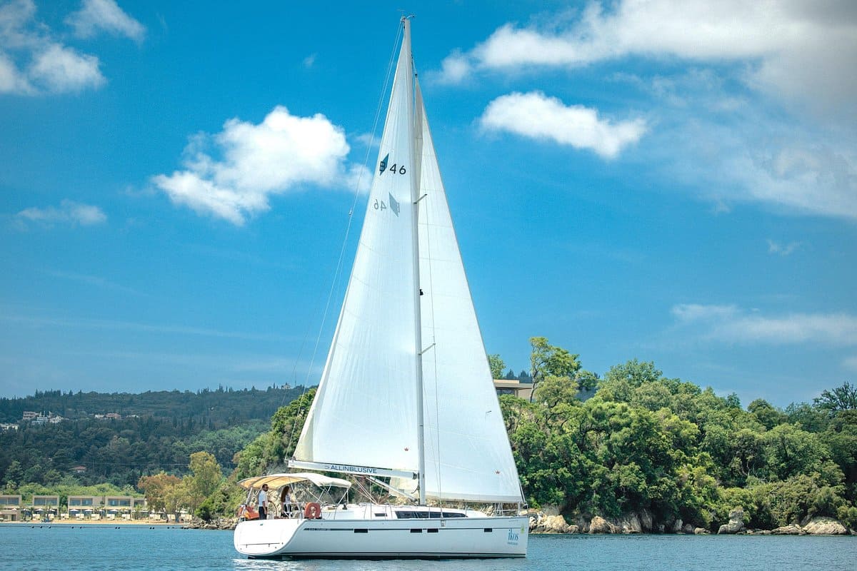 Corfu sailing tour yacht under full white sails off a wooded green shore of Corfu