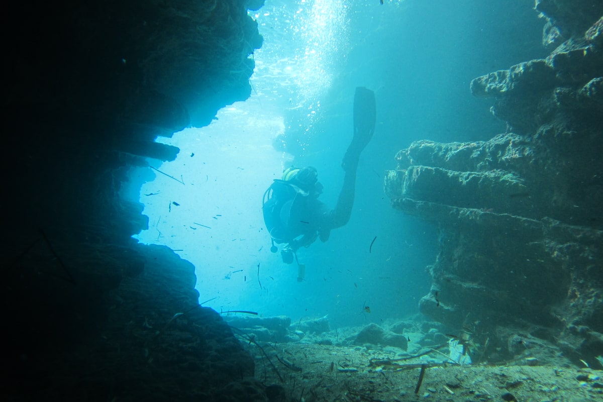 A Corfu scuba diving trip diver swims through a blue sea cave at Peristeres, lit from the open water