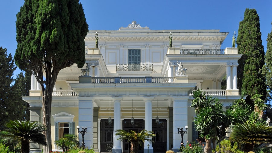 A Corfu tour stops at the white palace of the Achilleion among cypress and palm trees