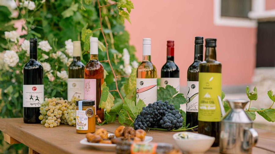 A Corfu wine tour tasting table with red, white and rose wine bottles, fresh grapes and small sweets