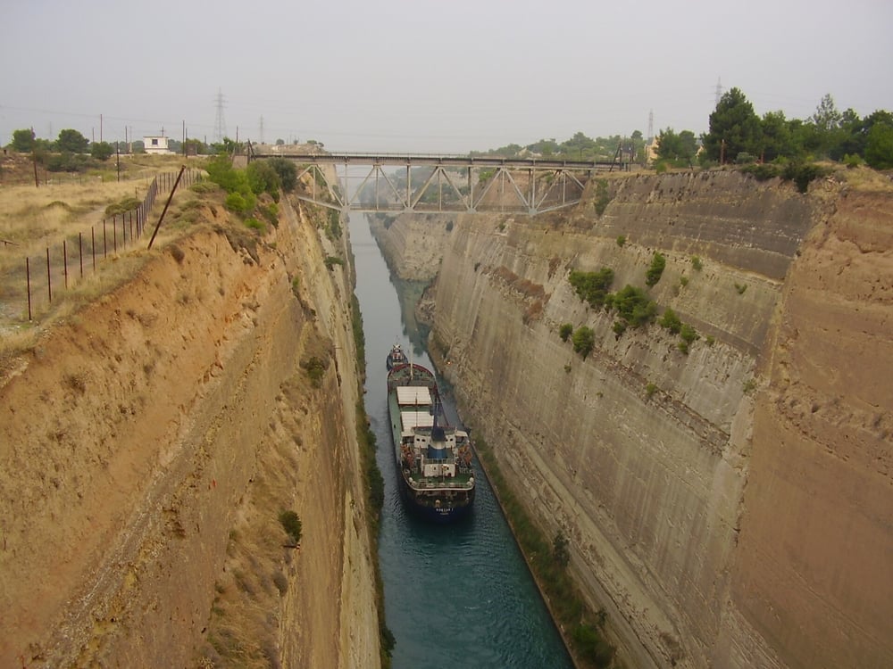 A Corinth Canal tour watches a ship towed between the steep walls of the canal