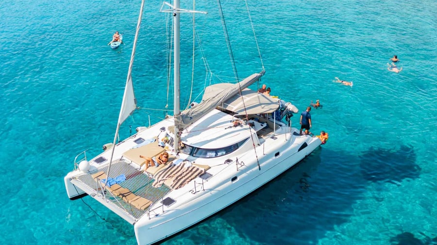 A Crete catamaran cruise anchors a white sailing catamaran in clear turquoise water while guests swim nearby
