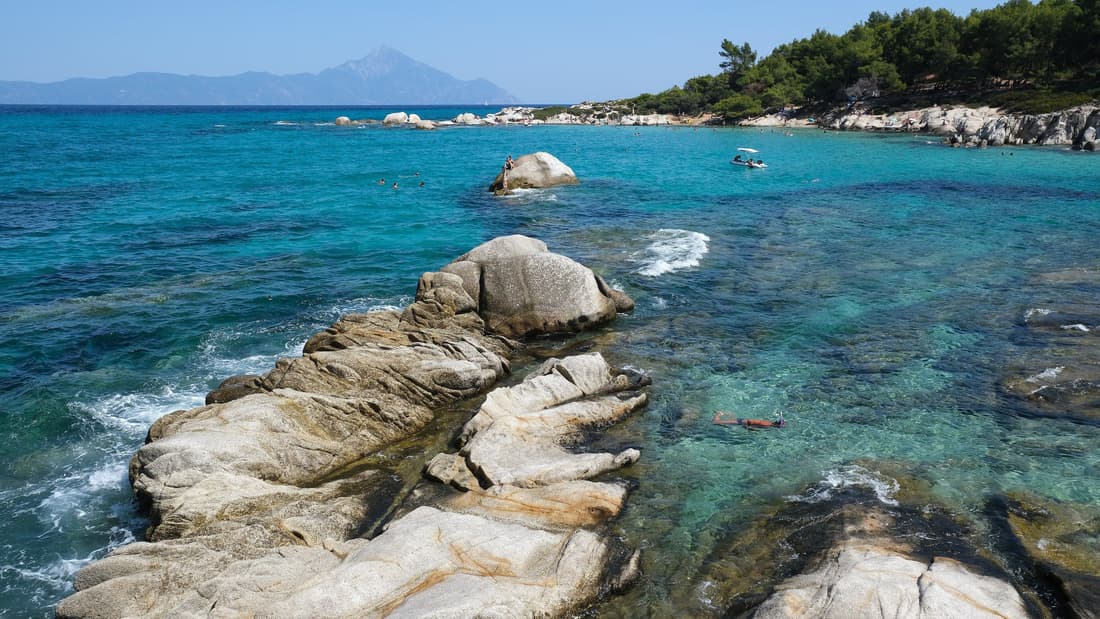 A Halkidiki boat tour reaches the turquoise water and smooth granite rocks of Kavourotrypes, with Mount Athos on the horizon