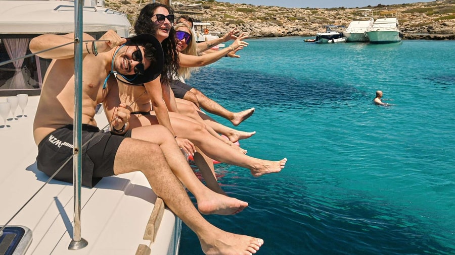 Friends sit on the bow of a catamaran above turquoise water in a cove of Dia during a Heraklion boat trip