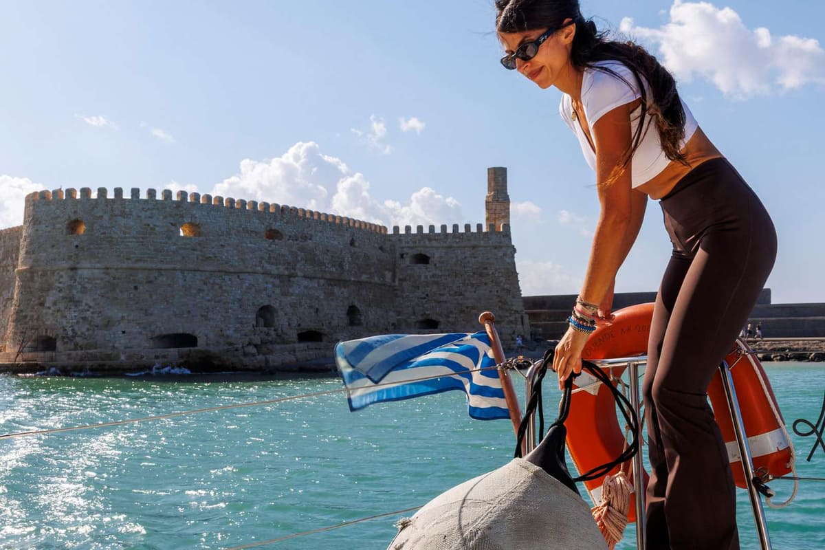 Heraklion sailing tour boat leaving the old harbour past the Venetian Koules fortress with a Greek flag at the stern