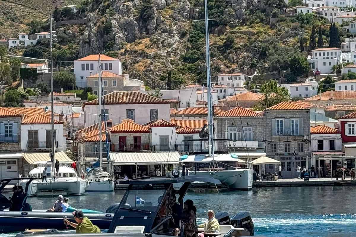 Hydra boat trip speedboat crossing Hydra harbour below stone mansions with red tiled roofs on the hillside