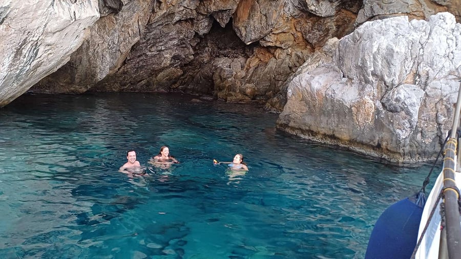 Swimmers float in clear water inside a rocky sea cave reached on a Hydra boat trip