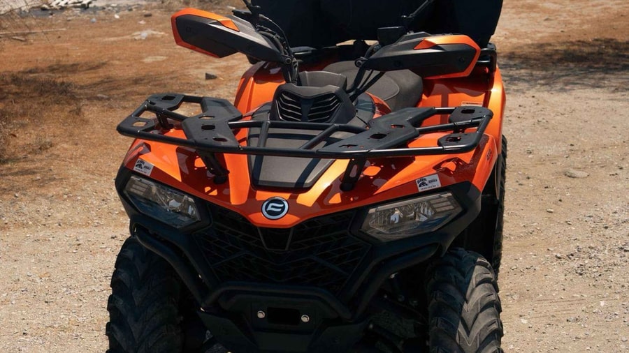 A Kos ATV tour quad bike in orange and black parked on a dry dirt track