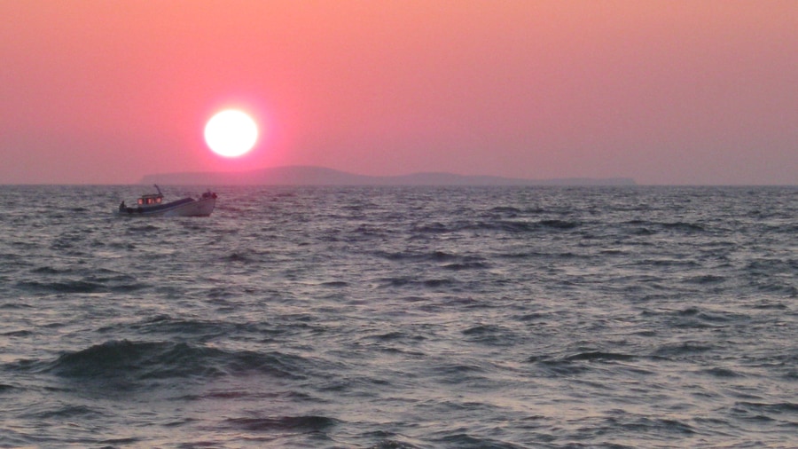 A small boat on the sea under a low pink sun off the coast of Kos on a Kos sunset cruise