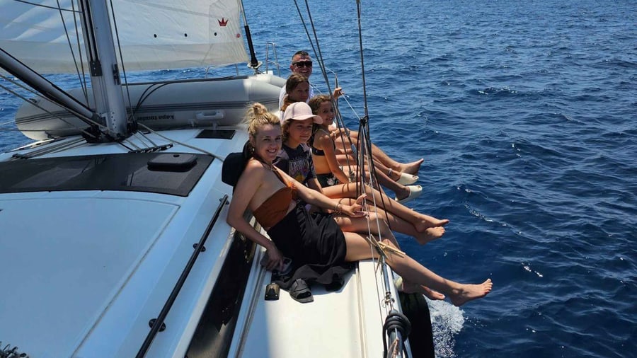 A Lefkada sailing tour runs with its sails full while guests sit along the bow above deep blue water