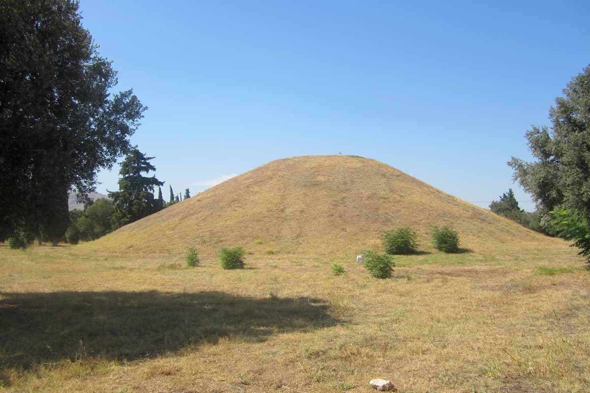 A Marathon tour stands before the Tomb of the Athenians, a large grassy burial mound on the plain of Marathon