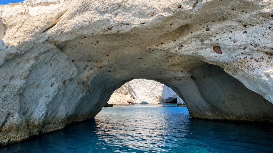 A white volcanic rock arch over calm blue water, a sea cave stop for Milos snorkeling