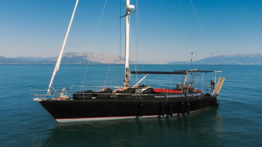 A Mykonos yacht cruise sailing yacht with a black hull rests at anchor in calm blue water