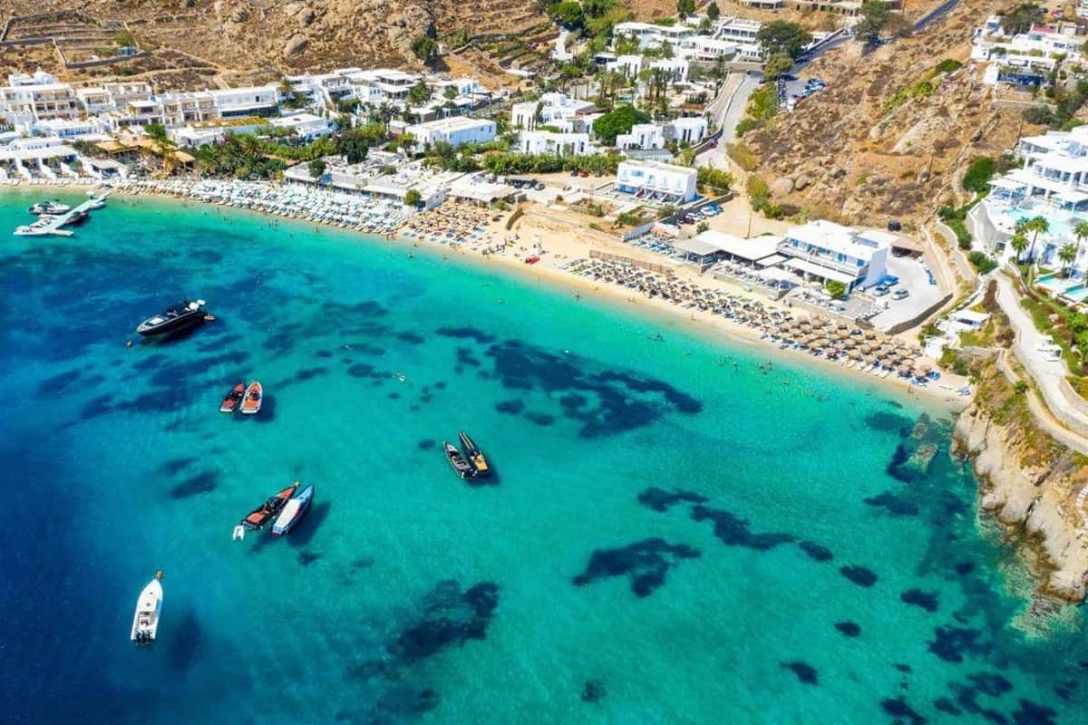A Mykonos yacht cruise stop where yachts and speedboats anchor in turquoise water off a south coast beach