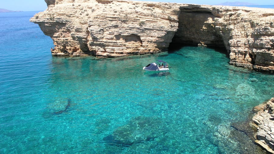 A Naxos boat trip anchors in clear turquoise water below the rock arches of Koufonisia