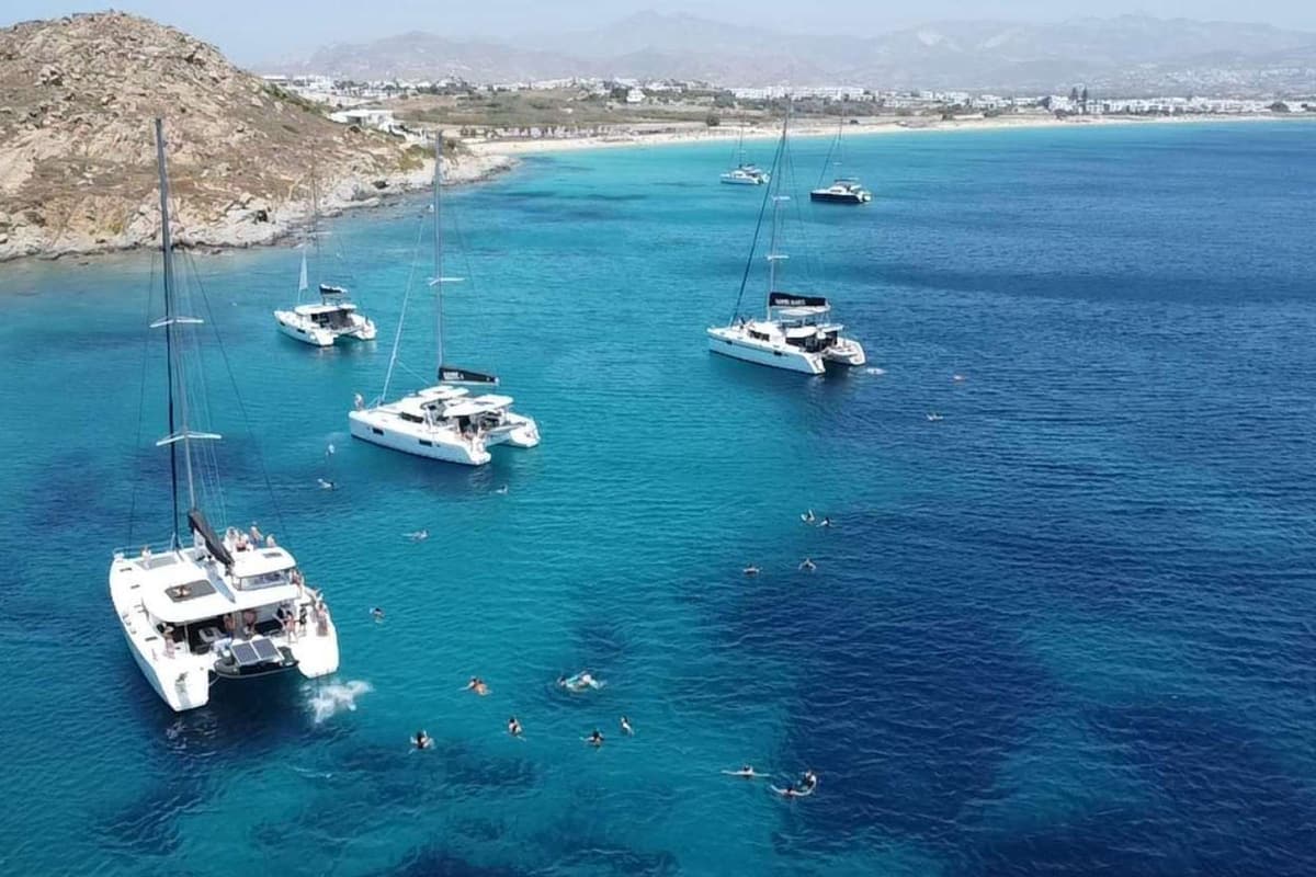 Naxos catamaran cruise boats anchored in blue water off a sandy west coast bay with swimmers in the sea
