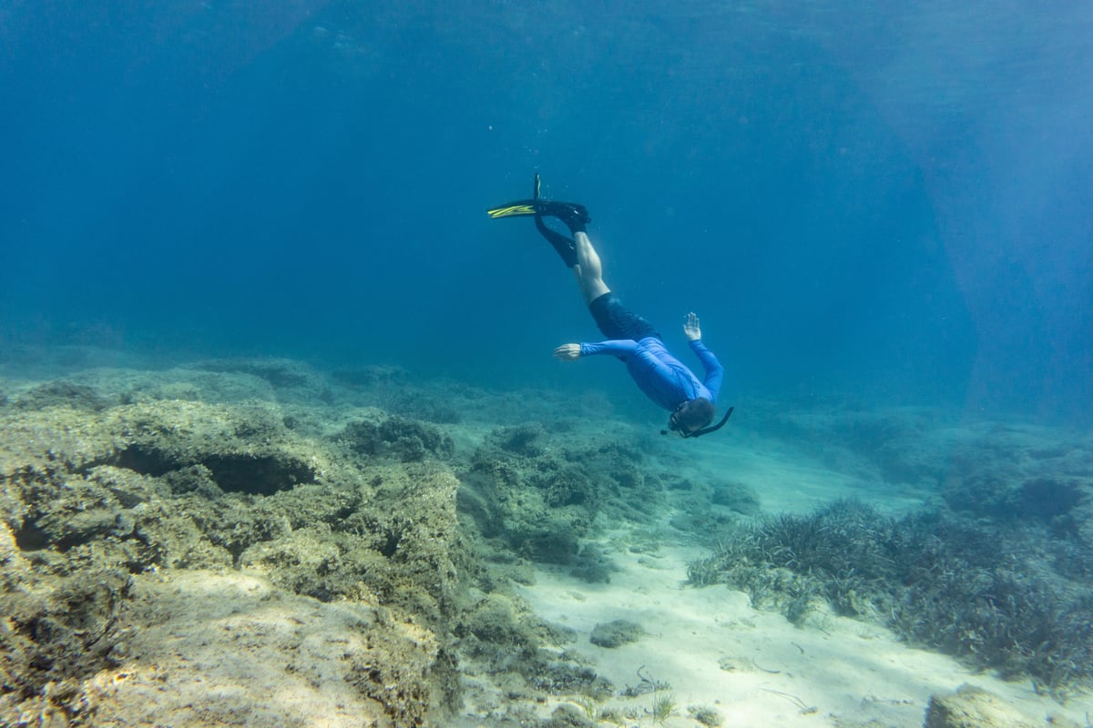 Naxos snorkeling free diver in fins glides down over a rocky seabed in clear blue water