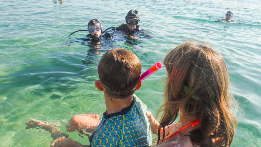 Two young snorkelers in masks sit in clear shallow water near the shore during Naxos snorkeling