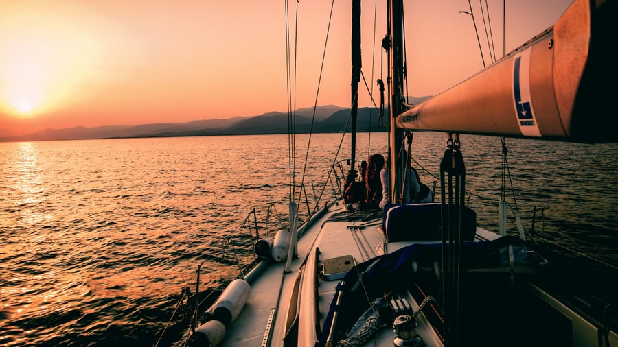 A sailing yacht deck at sunset on a Naxos sunset cruise, with the sun low over the hills