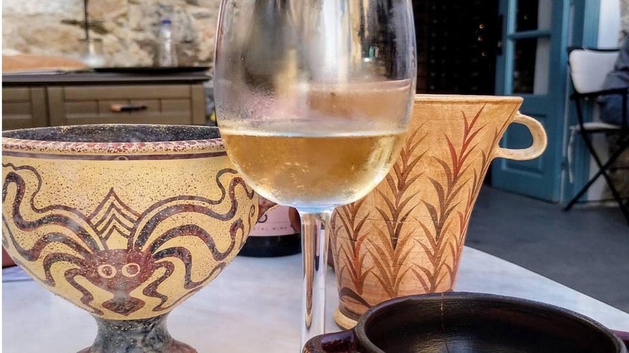 A glass of white wine between painted clay cups with an octopus pattern on a Naxos wine tour