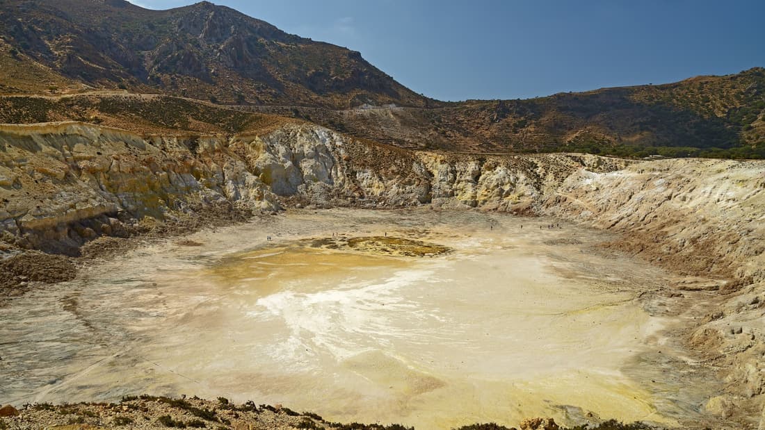 A Nisyros volcano tour looks down into the pale floor of the Stefanos crater under the caldera walls