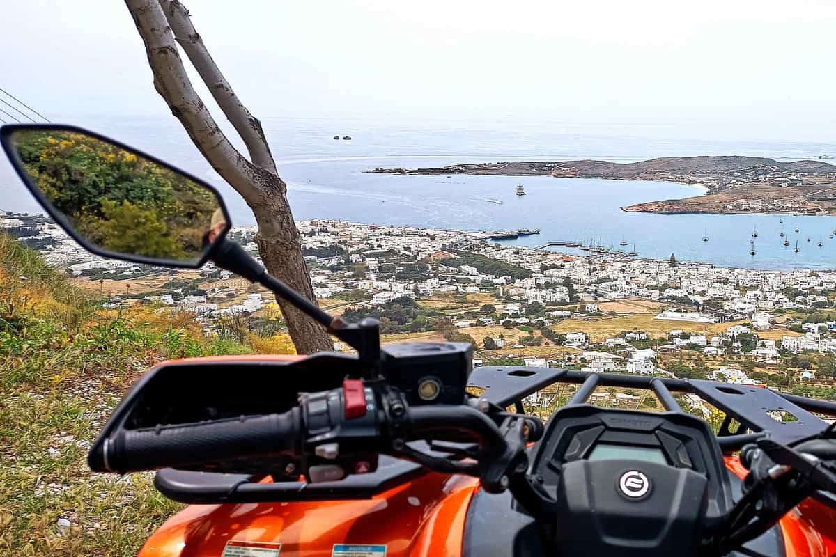 A Paros ATV tour stops a quad bike on a hill above Parikia, with the town and its wide bay below