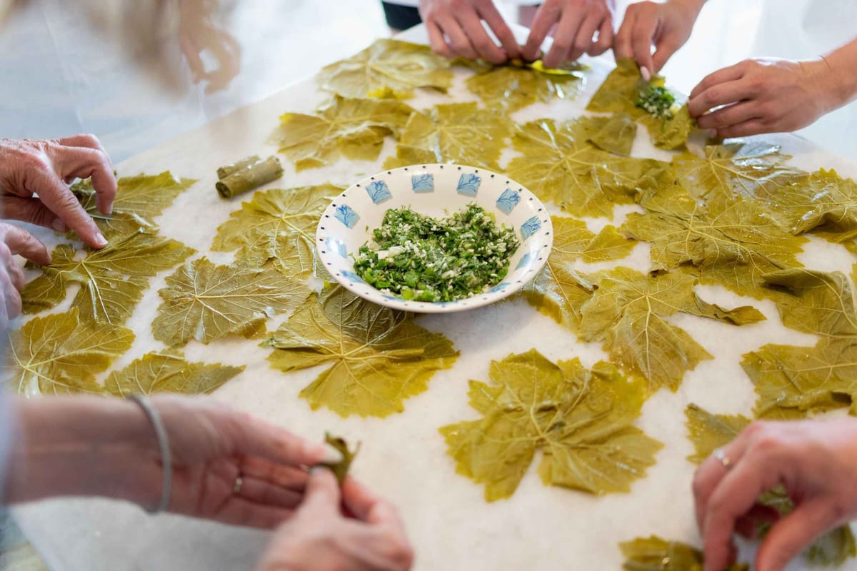 A Paros cooking class rolls dolmades by hand, with vine leaves spread over the table around a bowl of herb filling