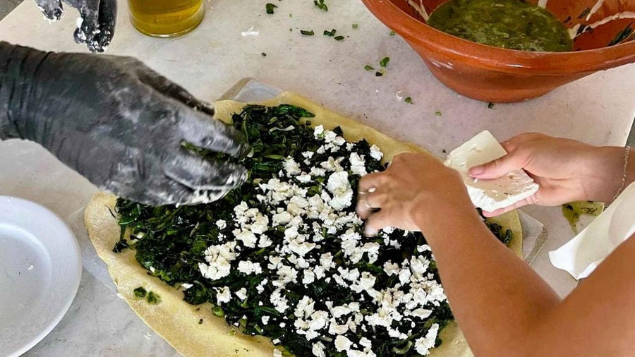 A Paros cooking class spreads wild greens and white cheese over a sheet of pastry to make a Greek pie