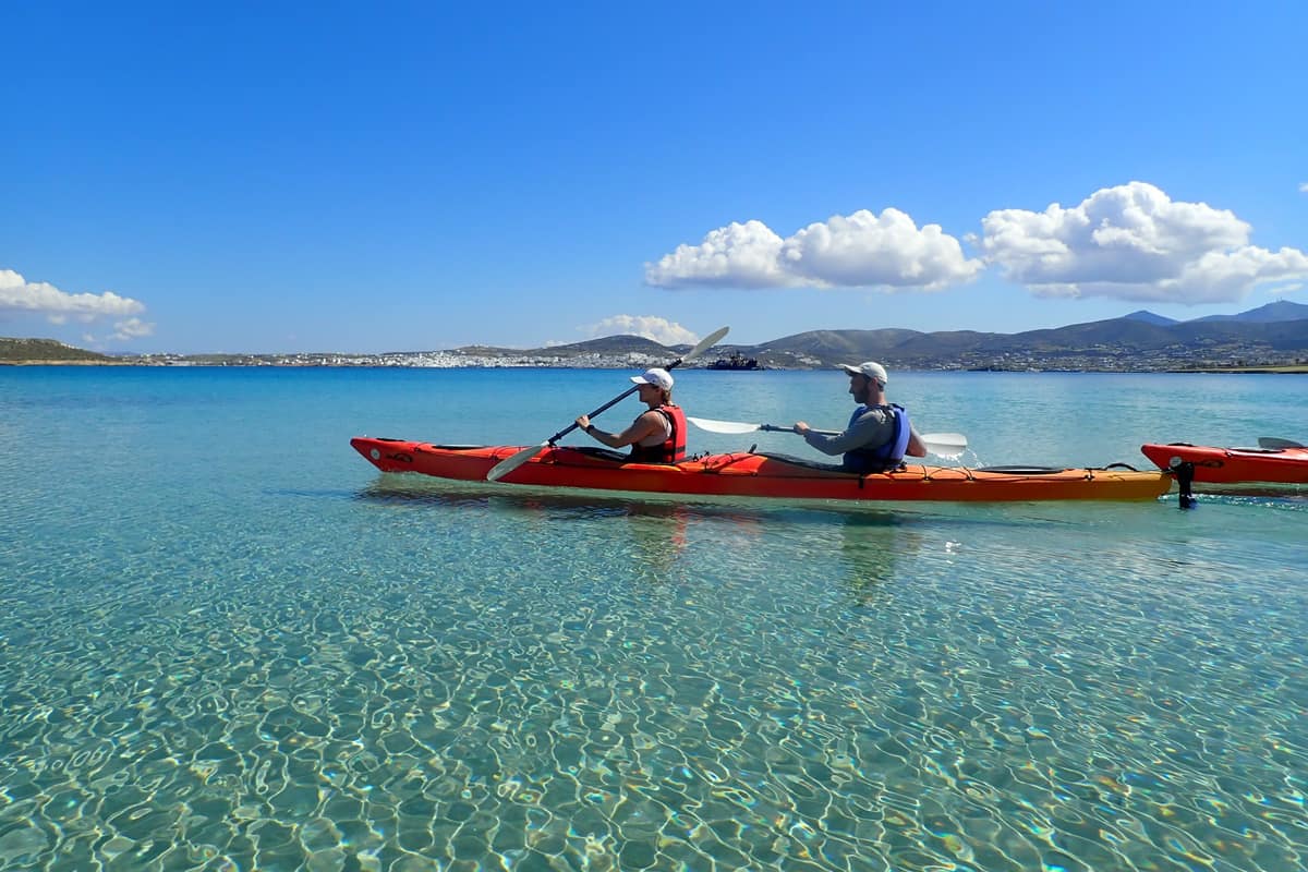 Paros kayak tour paddlers in a red tandem kayak glide over clear shallow water with the island coast behind