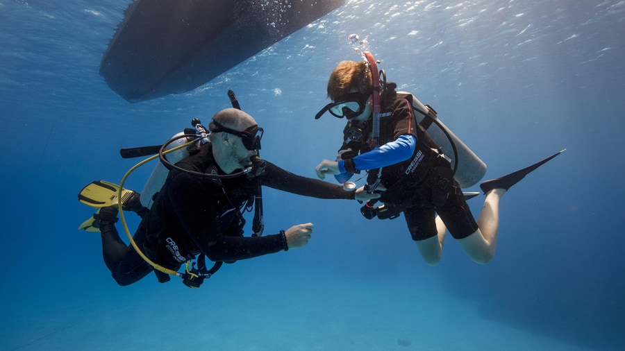 An instructor checks the gear of a student under the dive boat on a Paros scuba diving trip