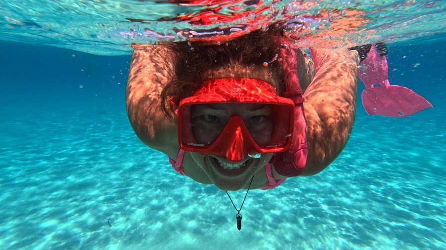A snorkeler in a red mask swims over white sand in clear water during Paros snorkeling