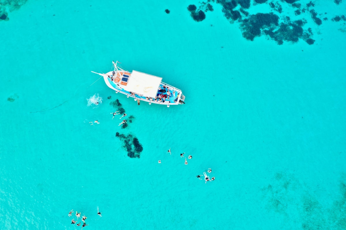 Paros snorkeling from a small boat anchored in turquoise water, with swimmers spread over sand and seagrass