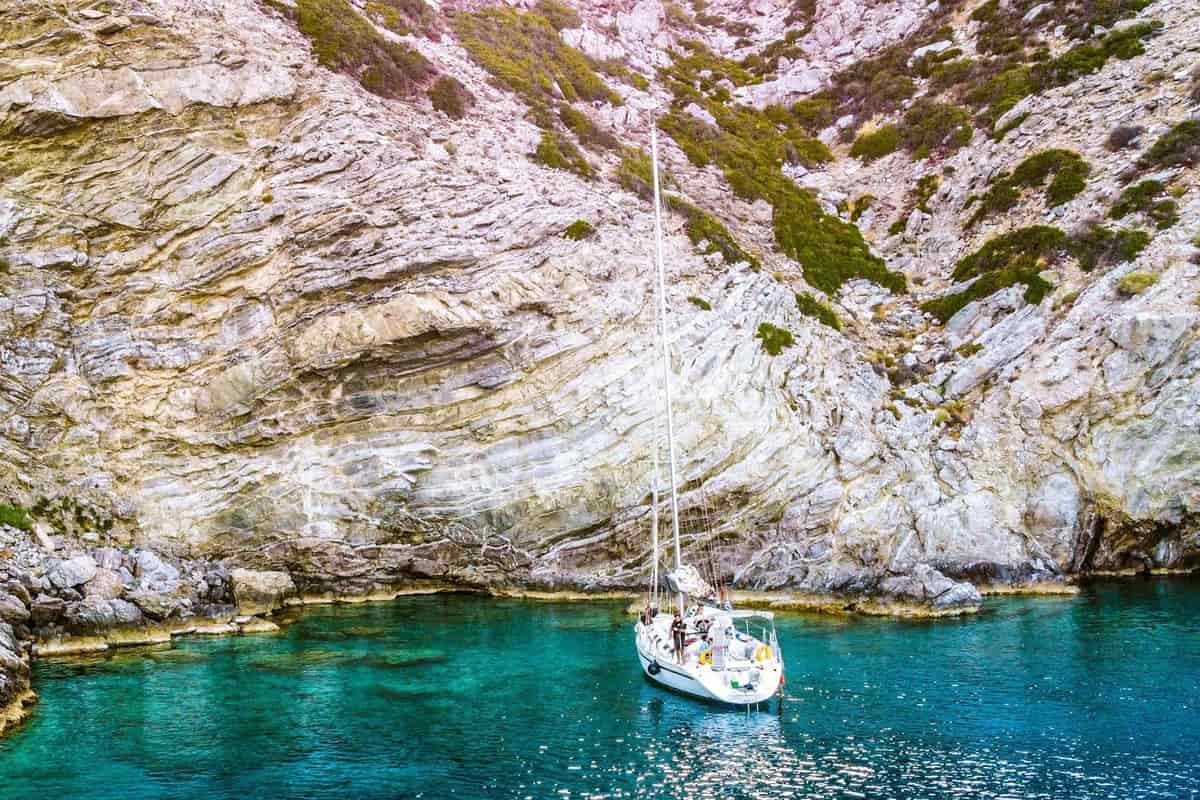 Sailing yacht at anchor in turquoise water below white layered cliffs on a Rethymno boat trip along the south coast of Crete