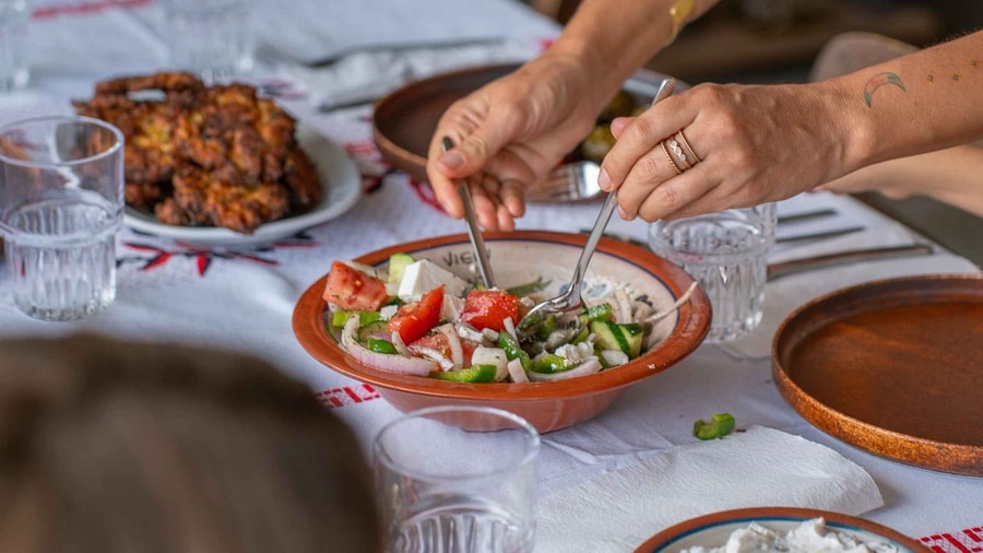 A Rhodes cooking class serves a village salad and fried fritters on a table laid with an embroidered cloth