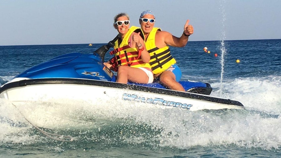Two riders in yellow life vests give a thumbs up on a Rhodes jet ski ride over choppy water