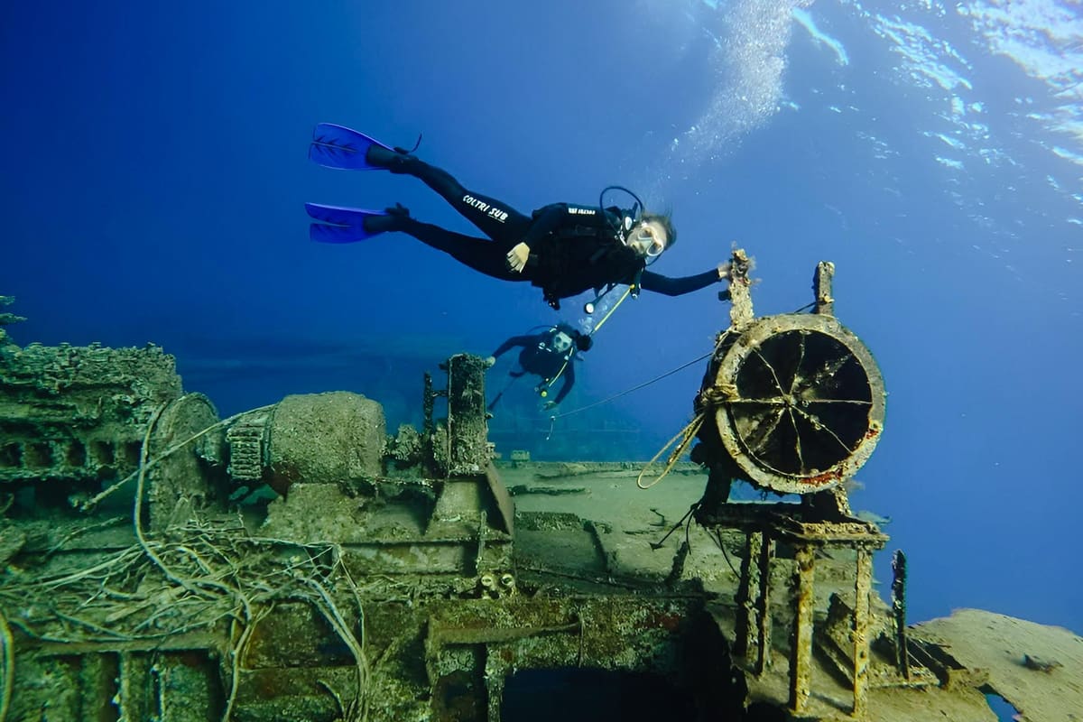 A Rhodes scuba diving trip diver swims over the rusted deck and machinery of a sunken wreck in blue water