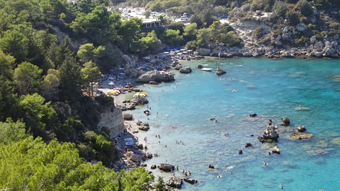 A Rhodes snorkeling tour swims the turquoise water of Anthony Quinn Bay between pine-covered slopes and rocks